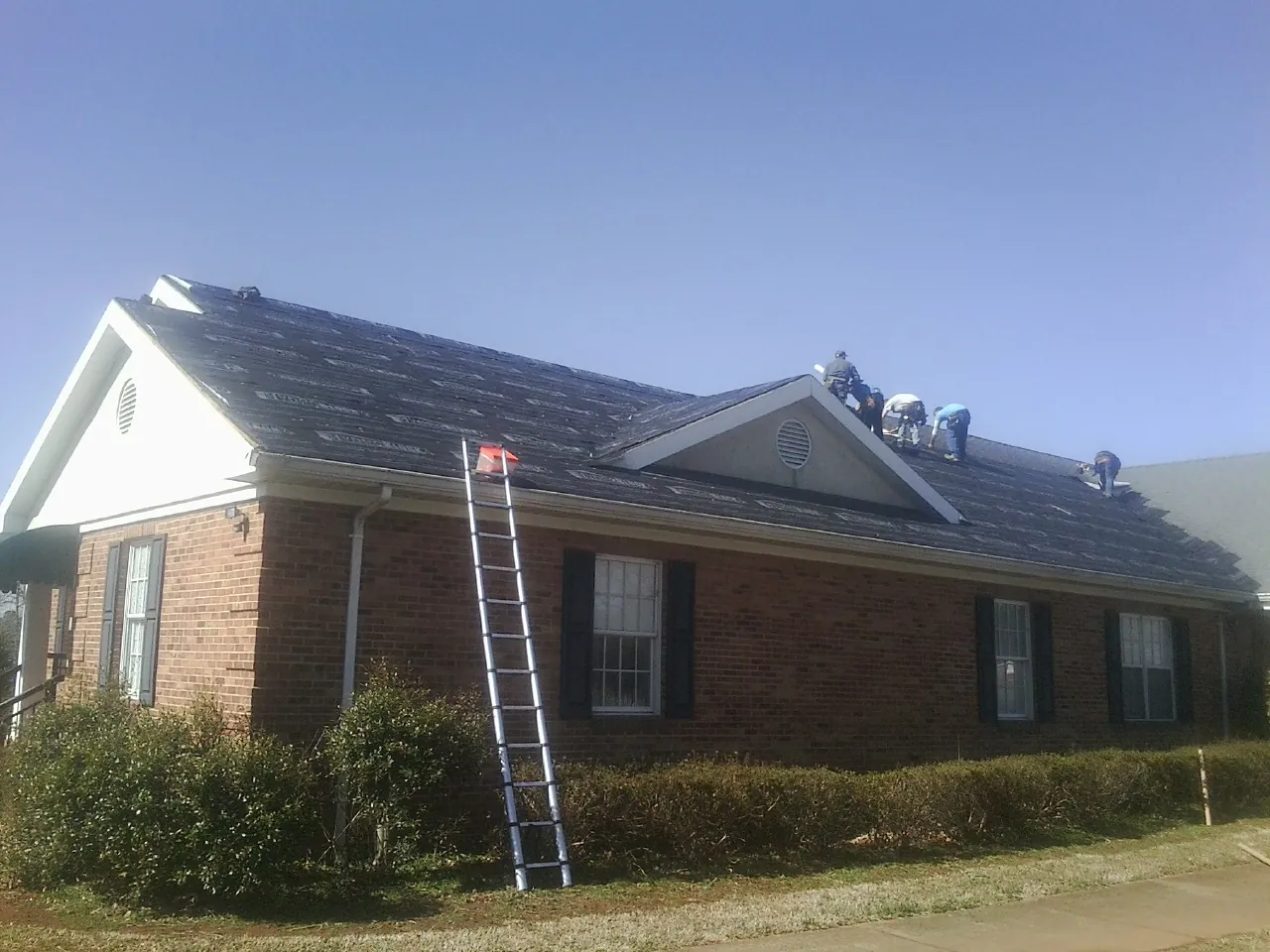 Crew tearing shingles off a brick ranch roof with a ladder set — Emergency Roof Repair work by our crew in Rushsylvania
