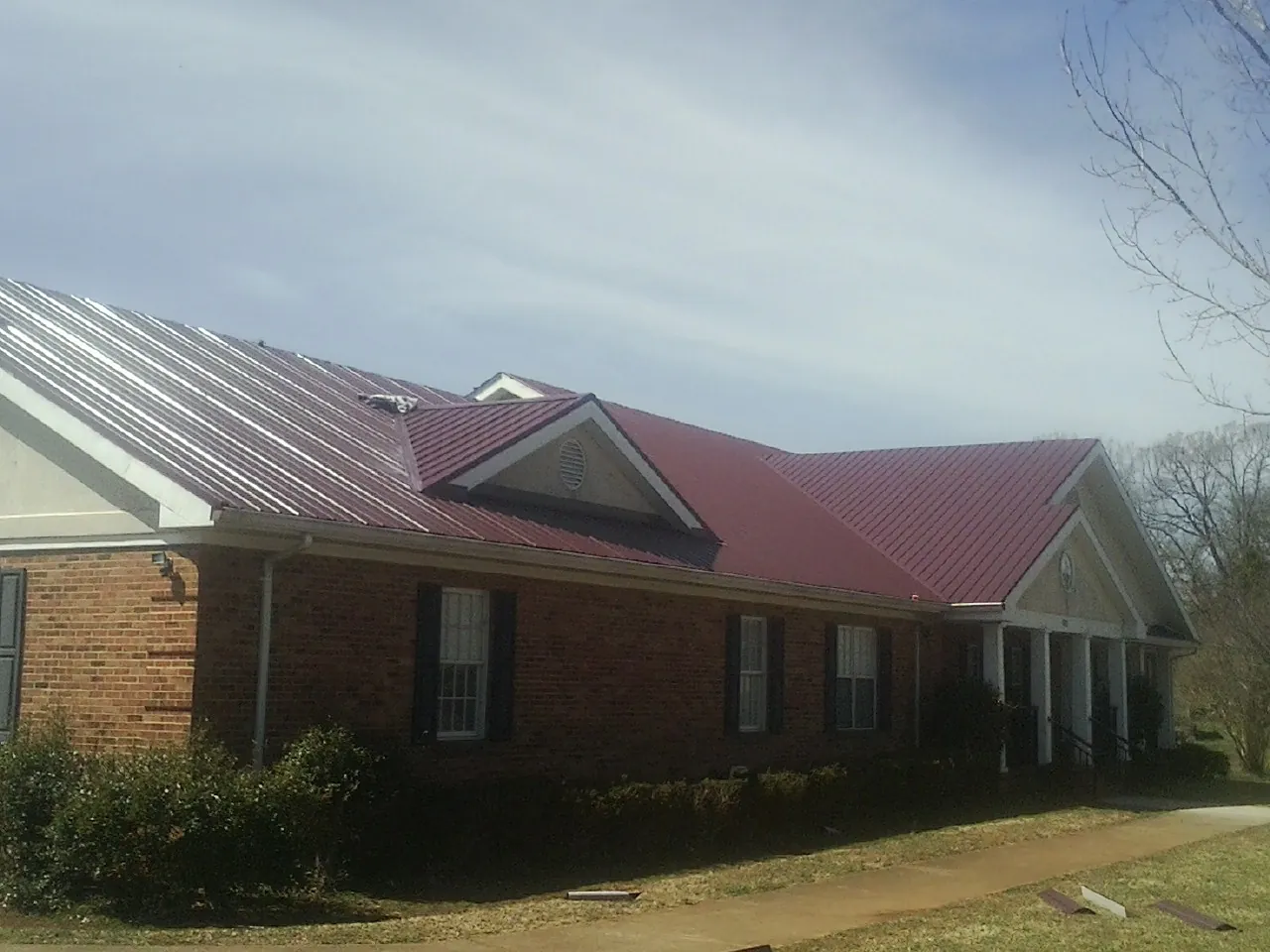 Red metal roof with gabled entries on a long brick building, from a Hail Damage Roof Repair job in Rushsylvania