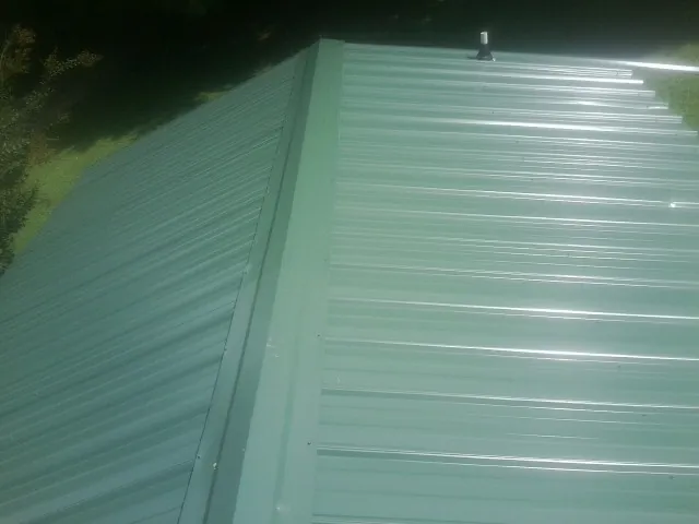 New green metal panels meeting at the ridge of a roof — Flat Roof Repair work by our crew in Rushsylvania