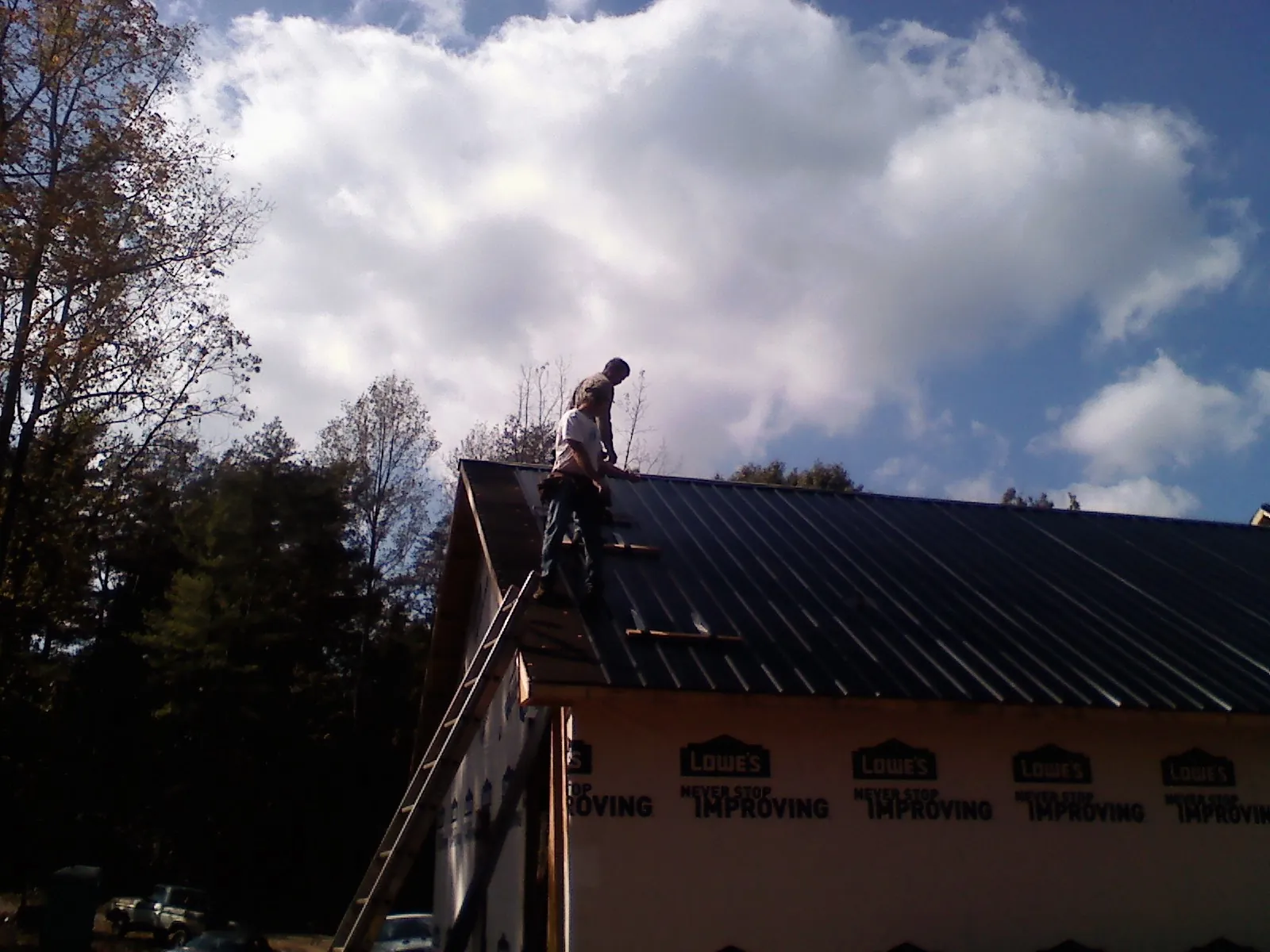 Roofer fastening dark metal panels high against a cloudy sky, from a Roof Inspection job in Rushsylvania
