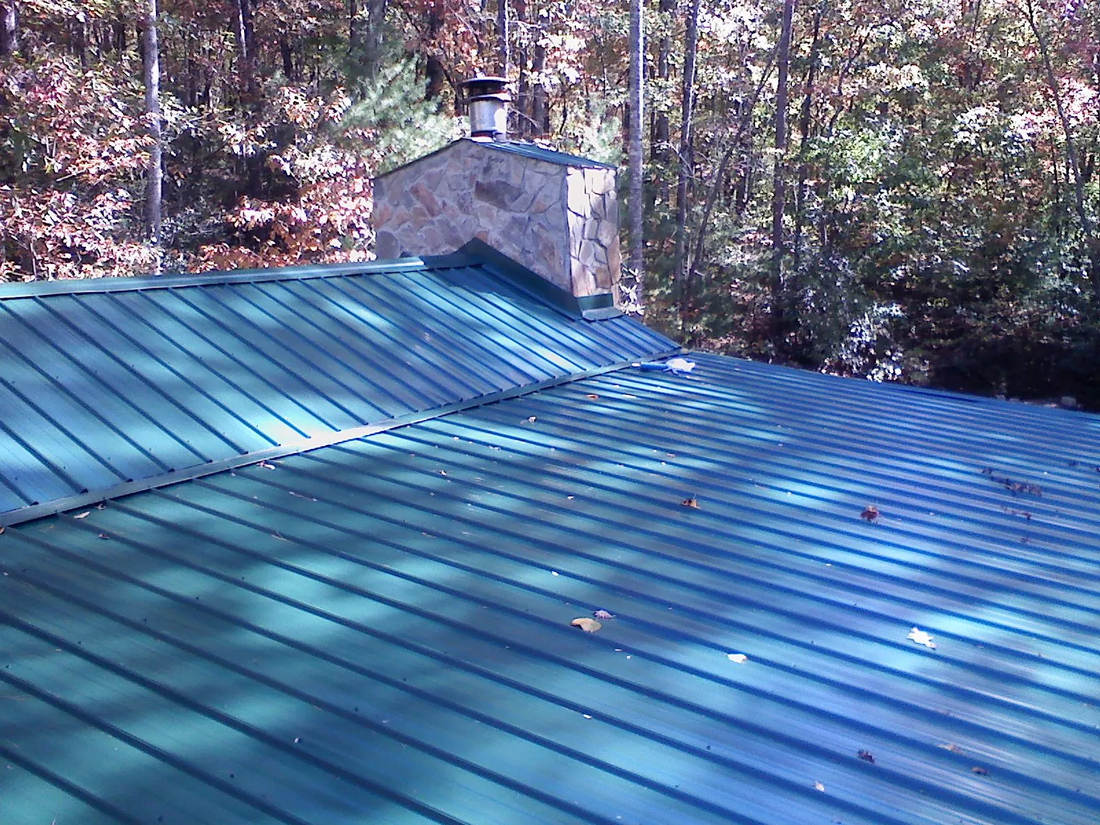 New green metal roof and stone chimney surrounded by autumn woods in Rushsylvania